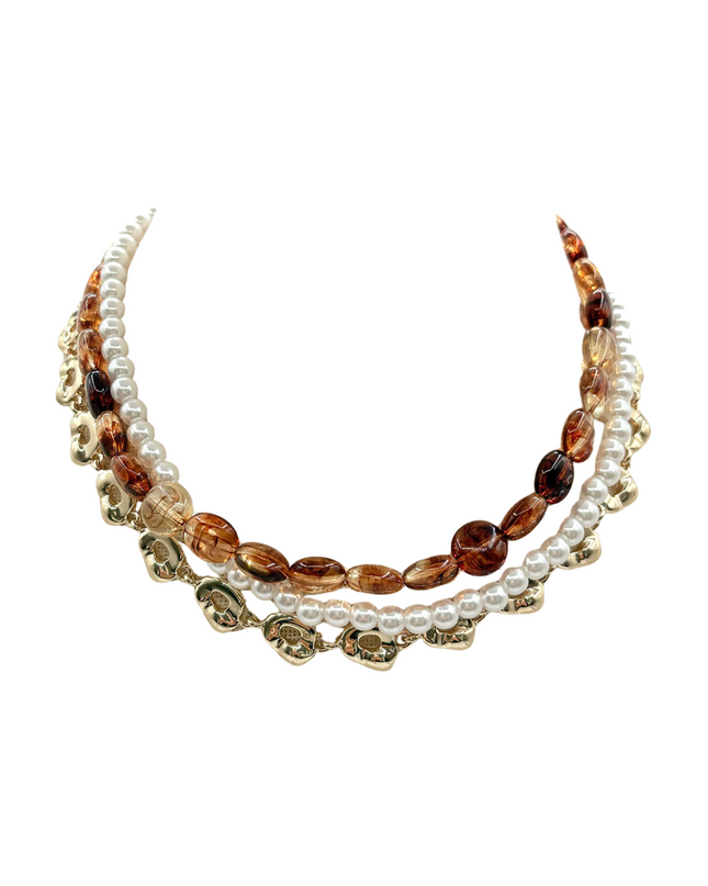 A multi-strand statement necklace featuring white faux pearls, translucent amber glass beads, and gold-toned floral charms, displayed on a clean white background.