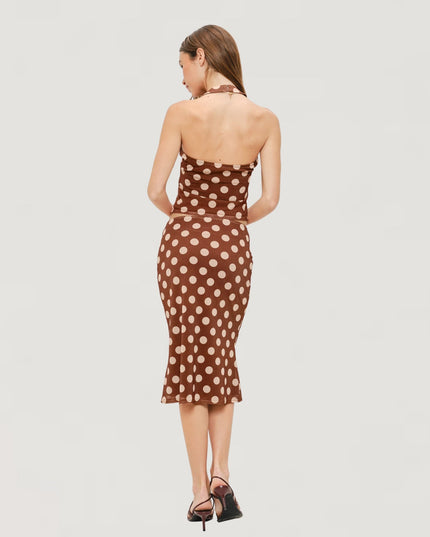 A woman is shown from the back wearing a brown halter-neck midi dress with a beige polka dot pattern, paired with black high-heeled sandals, against a light gray studio background.