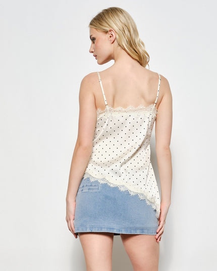 A woman shown from the back wearing a white spaghetti-strap camisole top with black polka dots and lace trim, paired with a light blue denim mini skirt, against a plain light gray studio background.