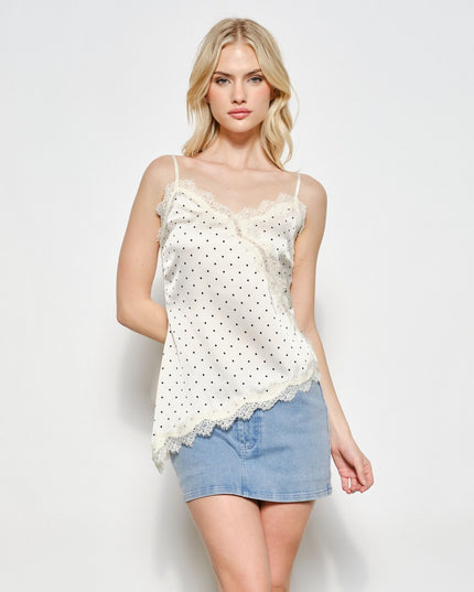 A blonde model wearing a white eyelet camisole top with black polka dots and lace trim, paired with a light blue denim mini skirt, against a plain light gray background.