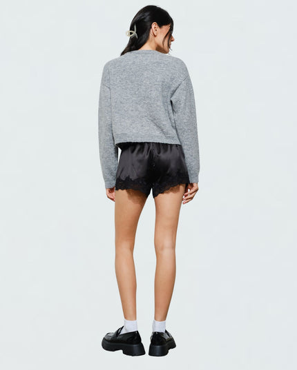 A model shown from the back wearing a gray cropped knit sweater, black satin shorts with a scalloped edge, white socks, and black platform loafers, against a plain light gray studio background.