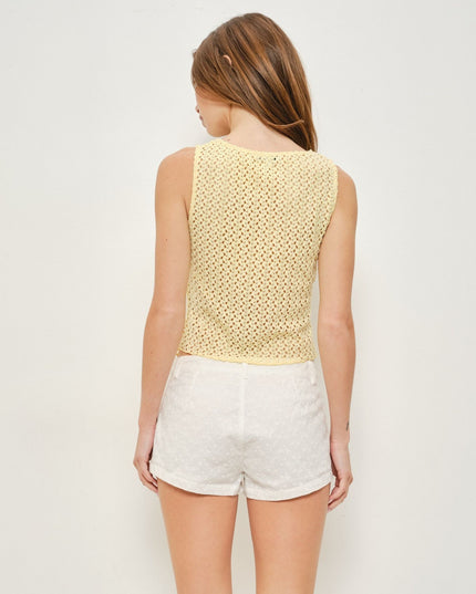 A woman shown from the back wearing a pale yellow open-knit sleeveless top and white shorts against a plain light background.
