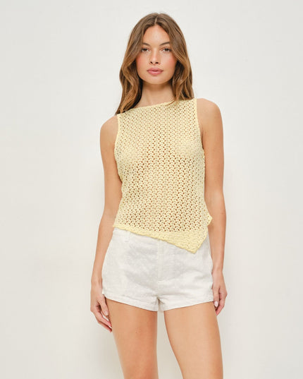 A woman modeling a pale yellow sleeveless crochet knit top with white shorts against a plain light gray studio background.
