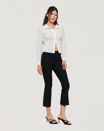 A model wearing a white cropped button-up shirt and black cropped pants with a small white polka dot pattern, paired with black heeled sandals, against a light gray studio background.