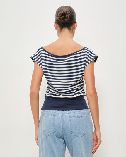 A woman viewed from the back wearing a navy and white horizontally striped boat-neck top with light blue jeans, set against a plain light gray studio background.