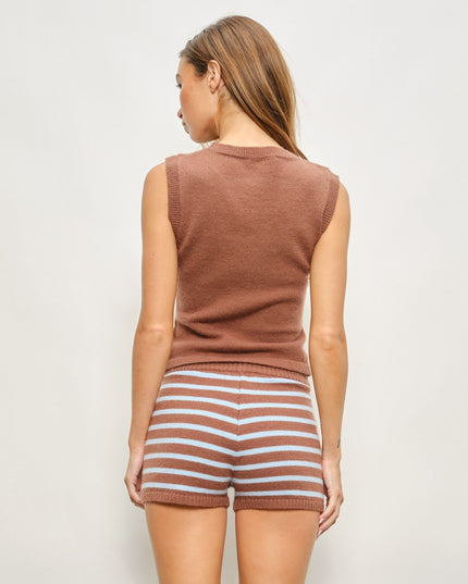 A woman shown from the back wearing a sleeveless brown knit top and brown-and-white striped knit shorts against a plain light gray studio background.