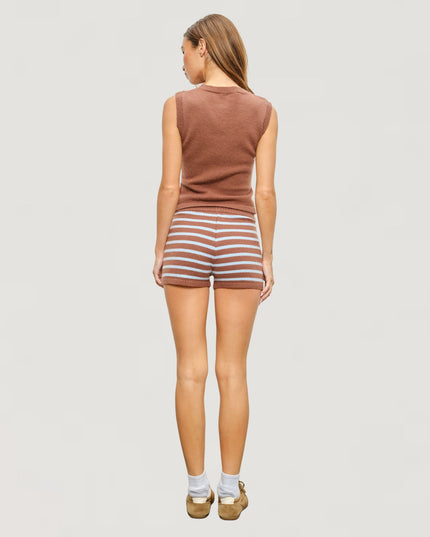A woman is shown from behind wearing a sleeveless brown knit top and brown and white striped shorts, standing against a solid light gray background.