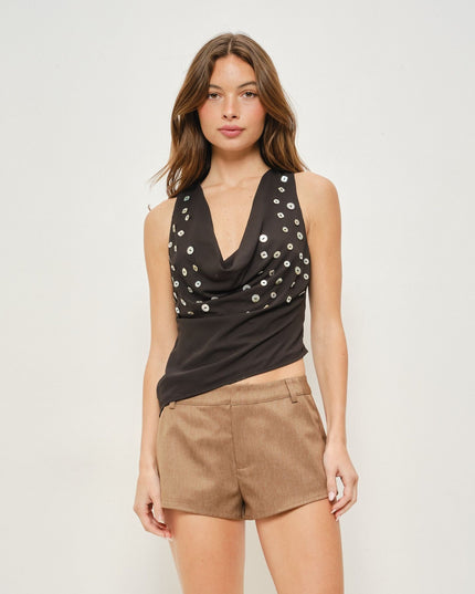 A woman modeling a black sleeveless cowl-neck top with silver sequin embellishments, paired with brown shorts, against a light gray studio background.