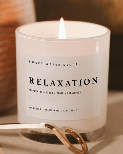 Candle labeled 'Relaxation' by Sweet Water Decor with a lit wick on a neutral background.