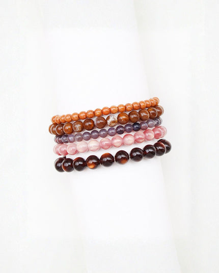 Four beaded stretch bracelets stacked together on a white background, featuring orange, brown, purple, and dark brown tortoiseshell beads.