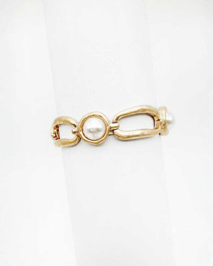A gold-tone ring featuring a textured barbell design with a central round white pearl and a small pearl accent on the side, displayed on a white ring stand.