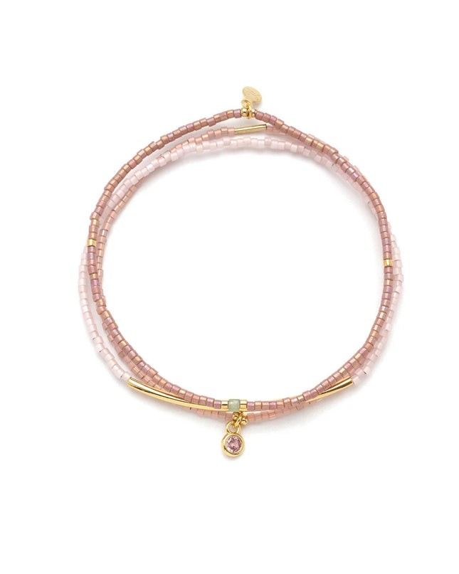 Pink beaded bracelet with gold accents on a white background