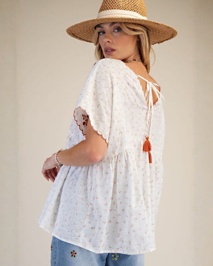 Woman wearing a white lace top with tassels and a straw hat on a plain background
