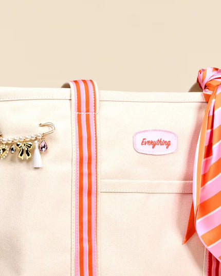 Beige pouch with orange and pink striped scarf, gold charm, and 'Everything' label on beige background