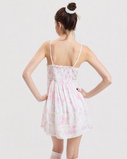 A woman shown from the back wearing a white spaghetti-strap mini dress with a pink abstract pattern, set against a plain light gray studio background.