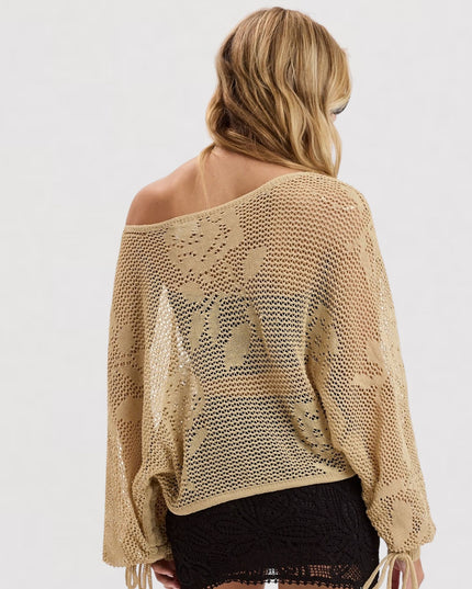 A woman shown from the back wearing a beige open-knit off-the-shoulder sweater over a black skirt, against a plain white studio background.
