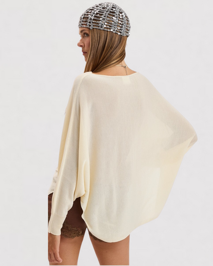 A woman shown from the back wearing a cream-colored, lightweight draped poncho-style top and a silver beaded headnet against a plain white background.