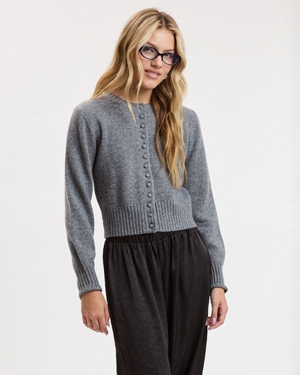 A woman modeling a gray knit cardigan with a button-down front, paired with black pants, against a plain white studio background.