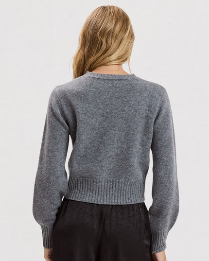 A woman viewed from the back wearing a heather gray knit sweater and dark pants against a plain light gray studio background.