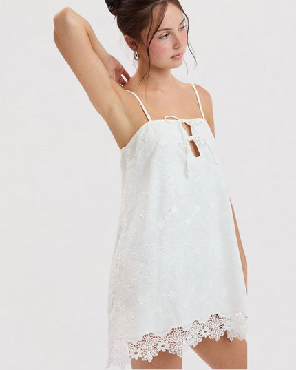 A woman modeling a white lace camisole nightgown with thin straps, a keyhole cutout at the chest, and a scalloped lace hem against a plain light gray background.