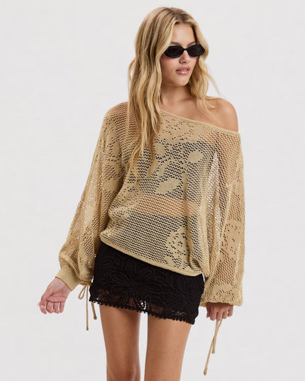 A woman modeling a beige off-the-shoulder crochet knit sweater with long sleeves and black lace shorts against a plain white studio background.