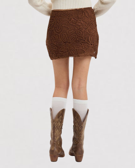 A person shown from the waist down wearing a brown textured crochet mini skirt, white knee-high socks, and brown cowboy boots against a plain white background.