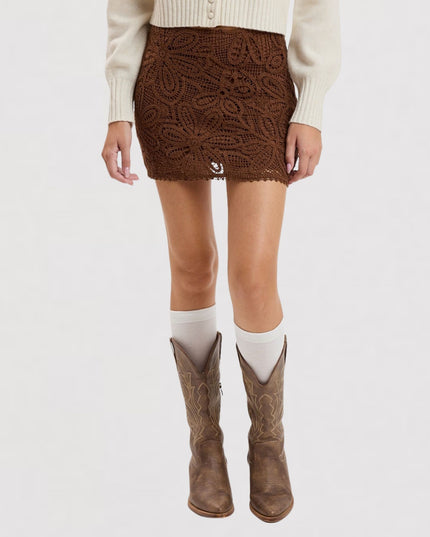A model from the waist down wears a brown lace mini skirt, white socks, and brown cowboy boots against a plain white studio background.