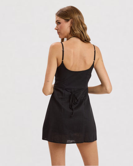 A woman wearing a black spaghetti-strap mini dress, shown from the back against a plain light gray studio background.
