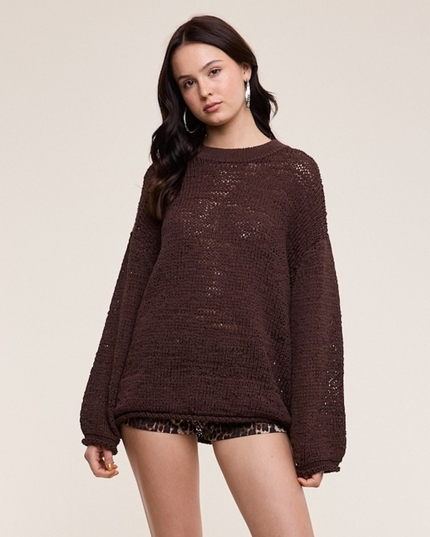 A woman modeling a dark brown, oversized textured knit sweater against a solid light beige background.