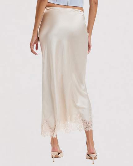 A woman wearing a satin midi skirt in a light champagne beige color with a lace hem, paired with beige high heels, shown from a rear three-quarter view against a plain white background.