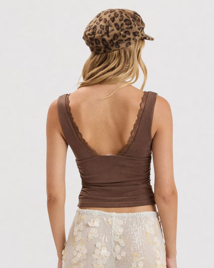 A woman shown from the back wearing a brown sleeveless ruched top with lace-trimmed straps and a leopard-print beret, against a plain light gray studio background.