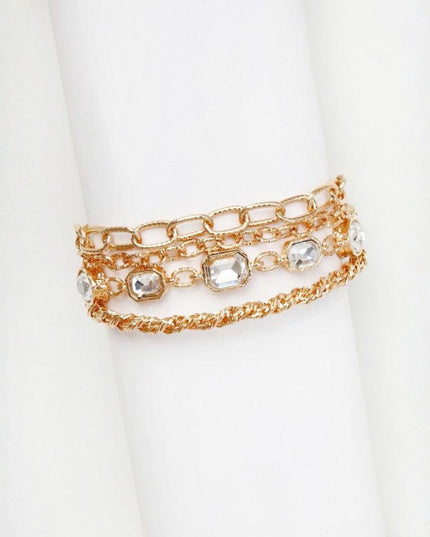 A stack of three gold-toned chain bracelets with clear rhinestone accents, displayed on a white cylindrical stand.