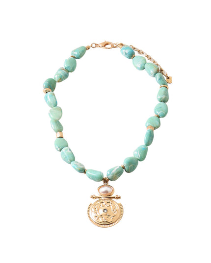 A beaded necklace featuring irregular light green turquoise-like beads separated by small gold spacer rings, with a gold-toned medallion pendant and a small white stone accent, shown on a plain white background.