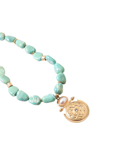 A beaded necklace featuring irregular light turquoise-green beads separated by small gold spacers, with a gold-toned coin-style pendant and a small pearl accent, shown on a plain white background.