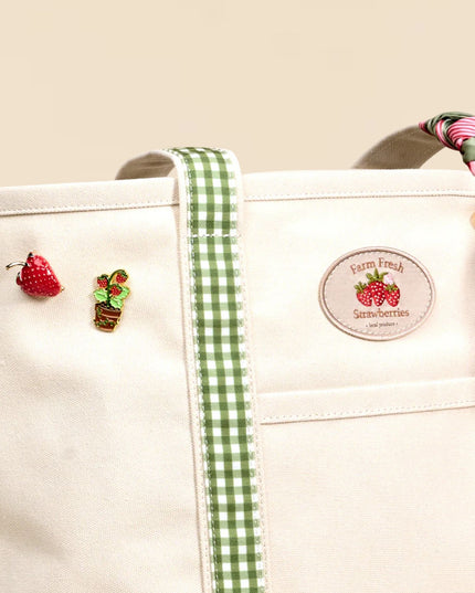 White tote bag with green ribbon, embroidered berries, and a label on a beige background