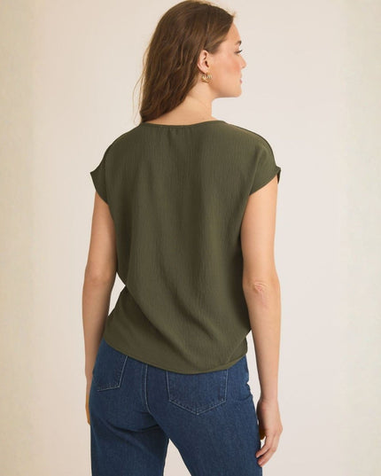 A woman shown from the back wearing an olive green short-sleeve top and blue jeans, standing against a plain light beige background.
