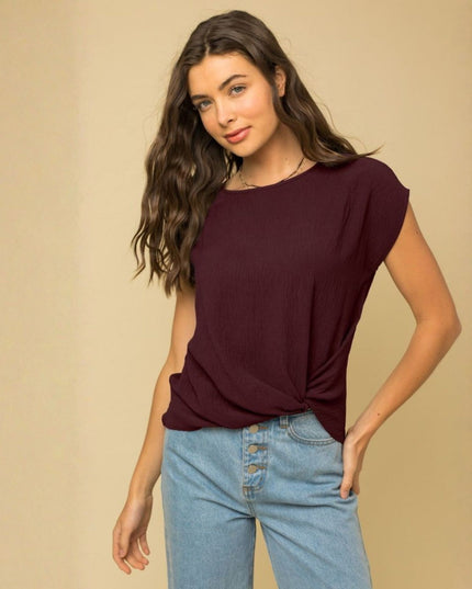 A woman modeling a short-sleeve boat-neck top in deep burgundy, paired with light-wash blue jeans, against a solid beige studio background.