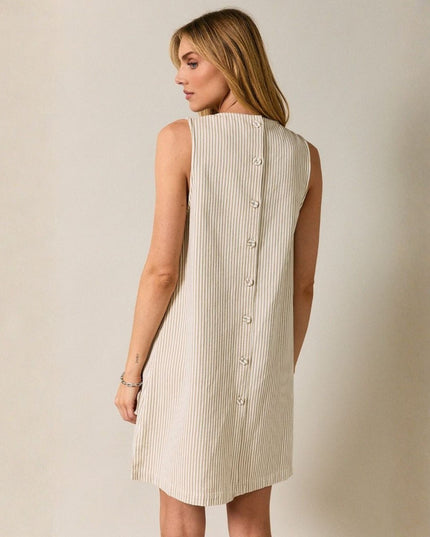 Woman wearing a sleeveless dress with buttons on a plain background