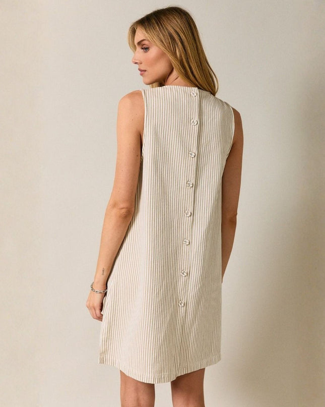 Woman wearing a sleeveless dress with buttons on a plain background
