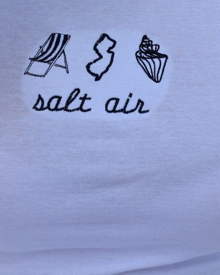 Close-up of a white fabric surface with black embroidered or printed beach-themed icons and the words 'salt air' in script.