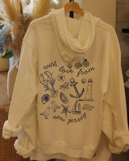 An off-white hooded sweatshirt with a cowl neck and rolled cuffs, featuring a navy blue graphic print with nautical illustrations and the text 'with love from new jersey' on the front, hanging on a wooden hanger.