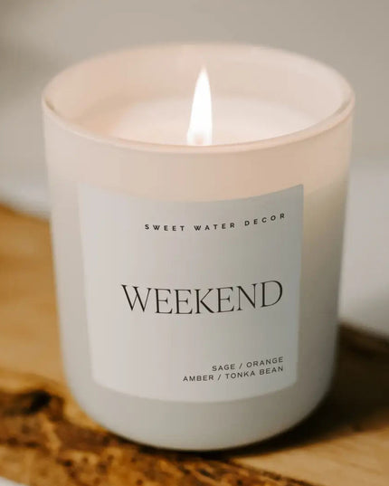 Candle labeled 'Weekend' by Sweet Water Decor on a wooden surface.