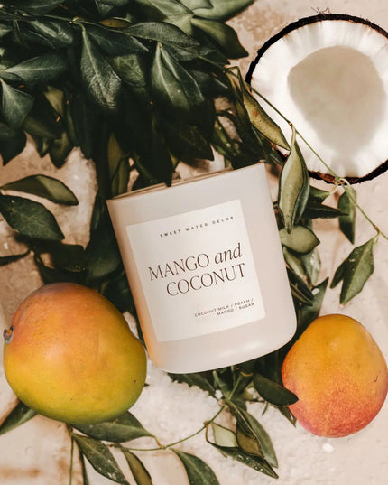 Candle labeled 'Mango and Coconut' surrounded by mangoes and a coconut on a leafy background