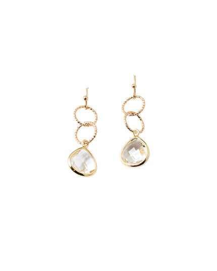 A pair of gold drop earrings featuring a textured circular ring, a smaller smooth ring, and a faceted teardrop-shaped clear gemstone, shown against a plain white background.