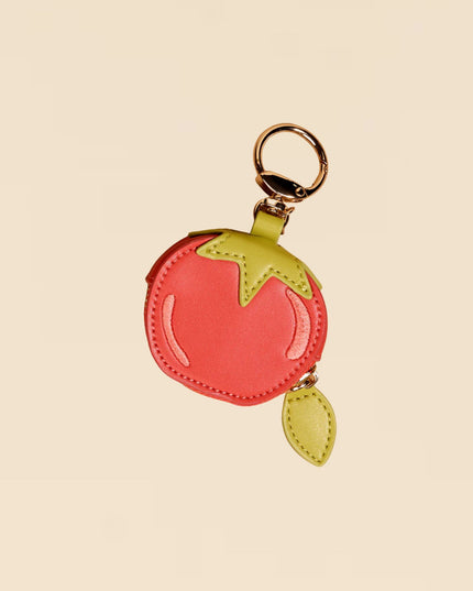 Keychain shaped like a tomato with a green leaf on a beige background