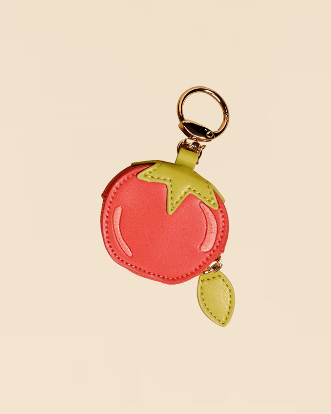 Keychain shaped like a tomato with a green leaf on a beige background