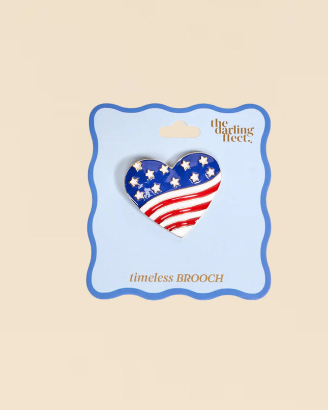 Heart-shaped American flag brooch on a 'The Darling Fleet' card against a beige background