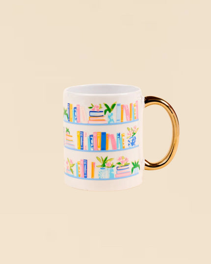 Mug with colorful book design and gold handle on a beige background