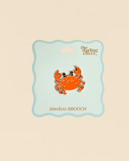 Orange crab brooch on a 'the darling effect' card against a beige background