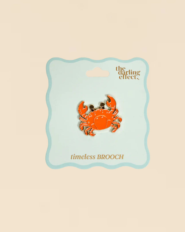 Orange crab brooch on a 'the darling effect' card against a beige background